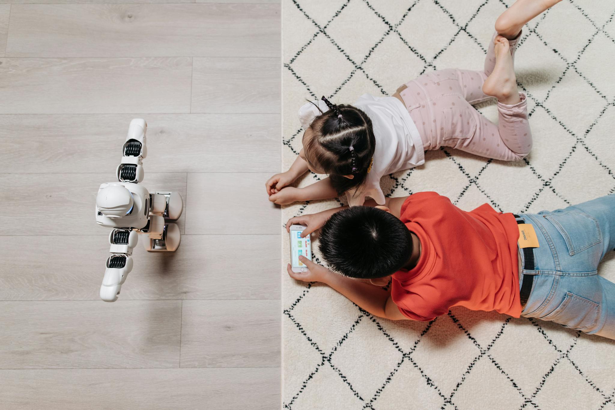 Two children interact with a robot on a carpet. Top view, educational technology concept.